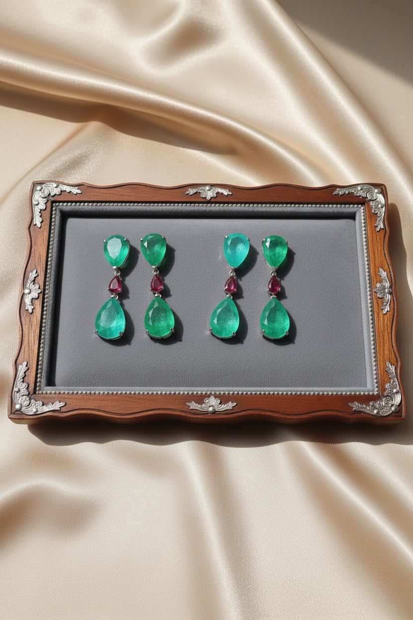 Set of emerald green teardrop earrings with red gemstones on a decorative tray.