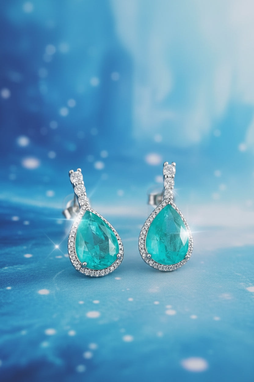 Teardrop-shaped emerald earrings with diamond accents on a stone architectural background