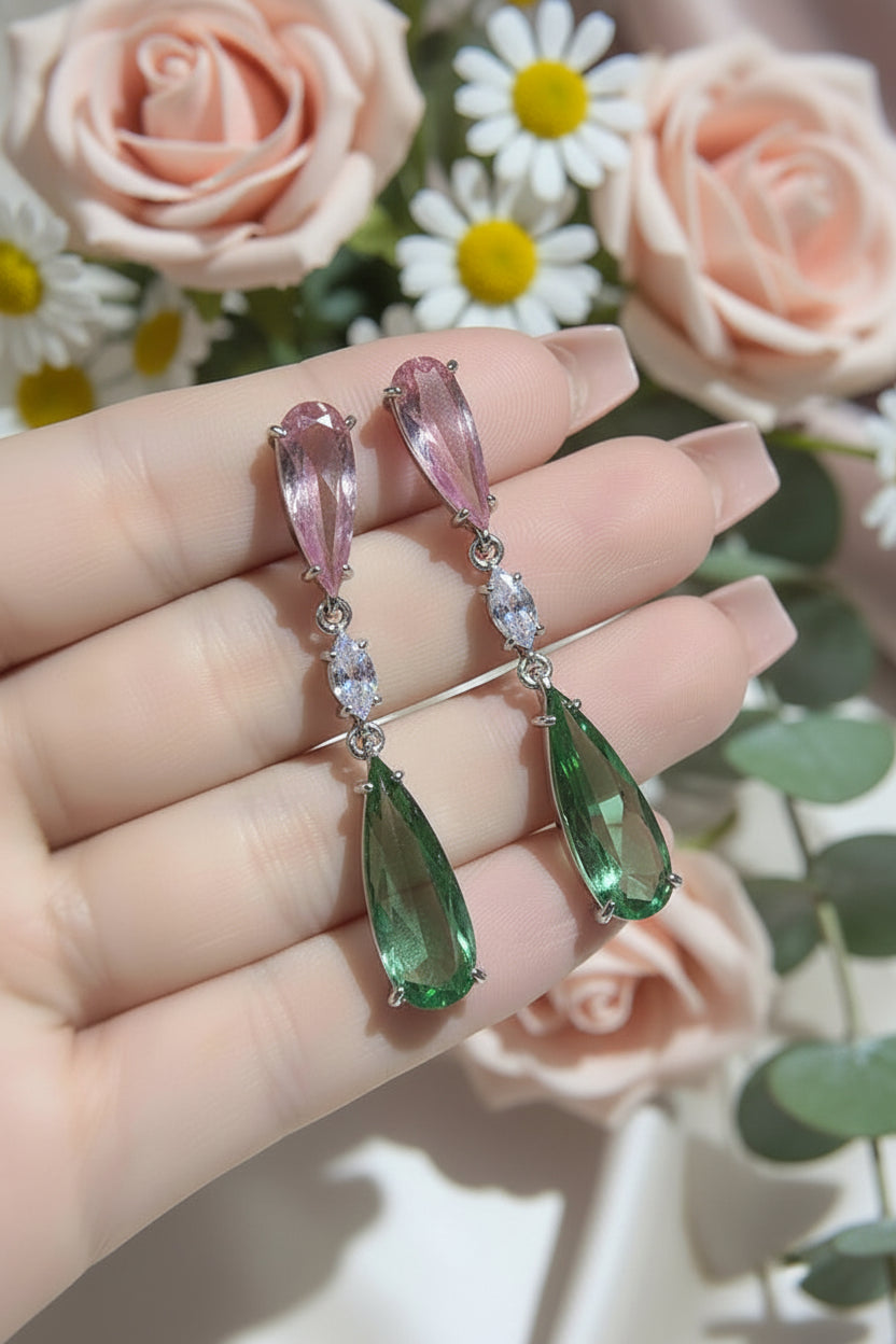 Long earrings with pink and green teardrop-shaped gemstones held in a hand.