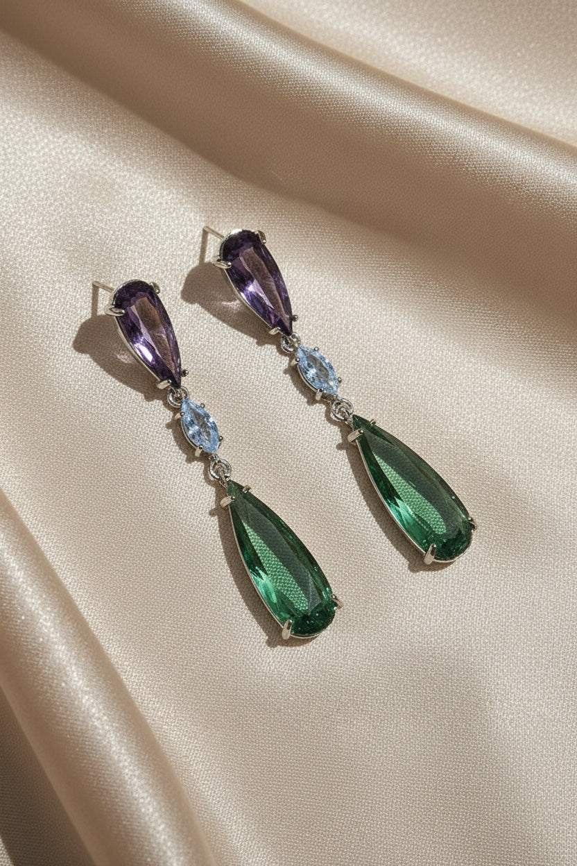 Pair of earrings with pink and green gemstones on a black cushion in a jewelry box.