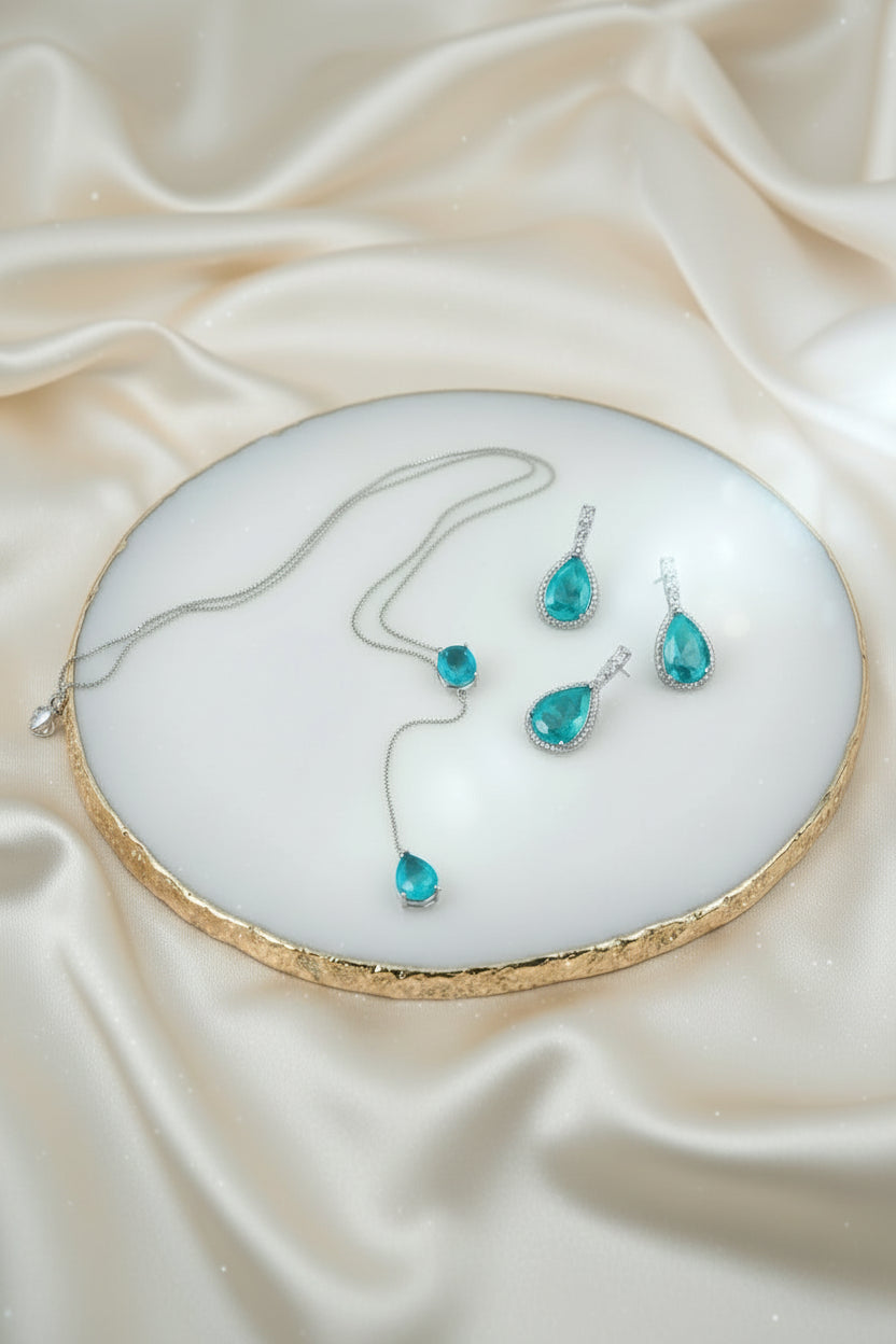 Teardrop-shaped turquoise gemstone jewelry set on a textured surface