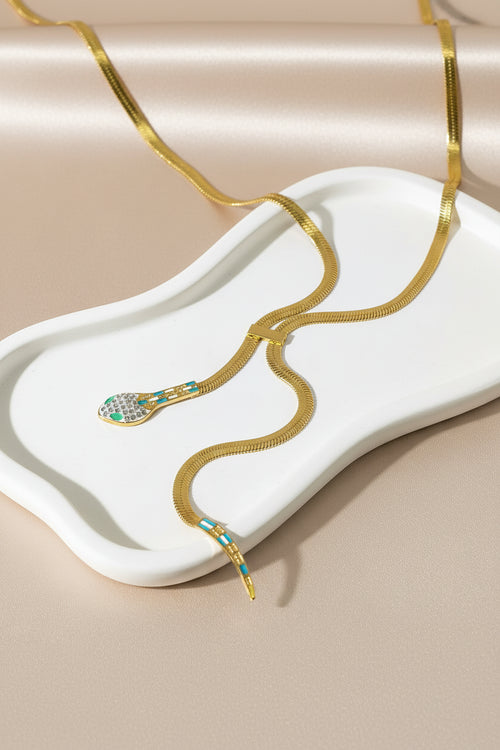 Gold snake-shaped necklace with gemstones on a marble surface