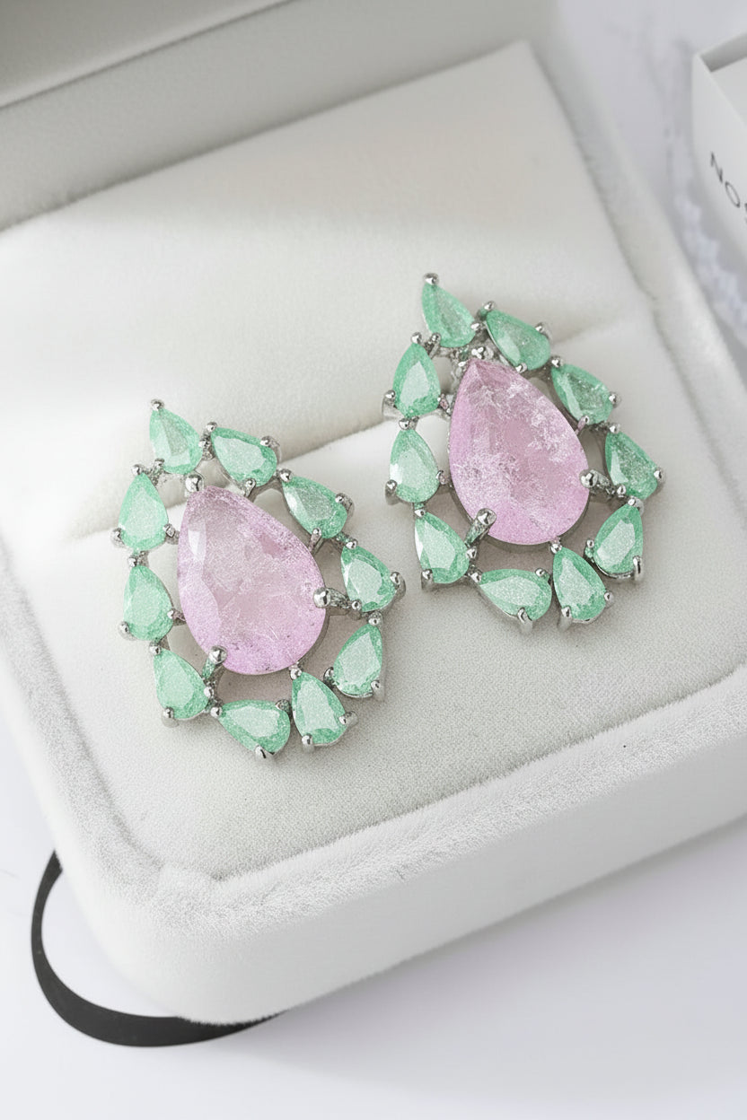 Pair of earrings with pink central stones and green teardrop stones on a white cushion.