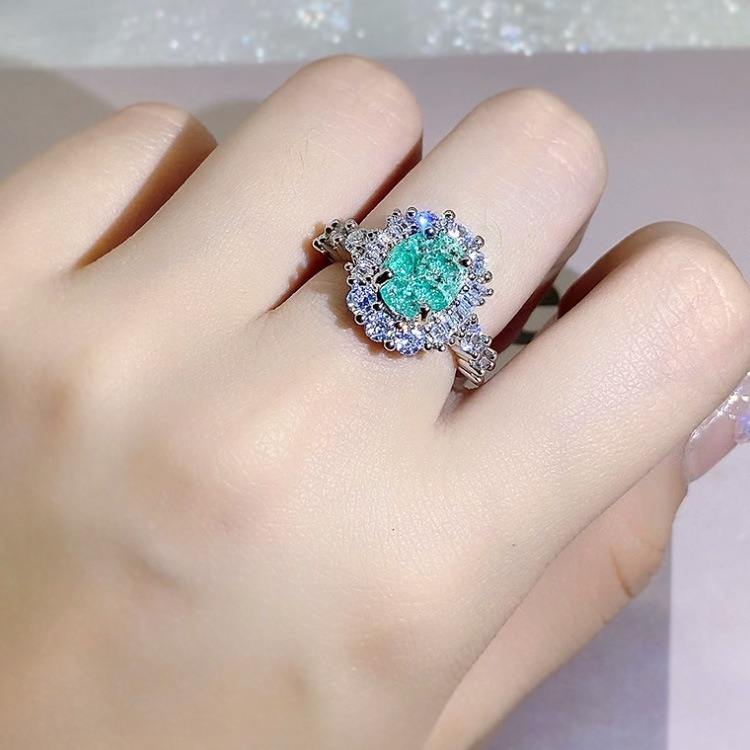 Ring with a green gemstone on a finger against a neutral background