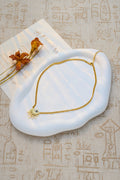 Gold necklace with a sun design on a white stone surface with dried flowers.